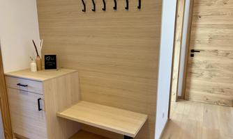 A modern entrance area with a wooden bench and hooks on the wall. A small table holds decorative items and a sign.
