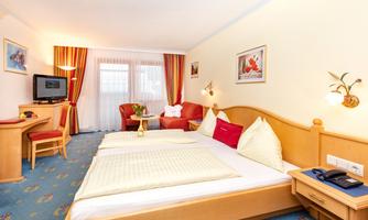 A cozy hotel room with two single beds, a desk, and a television. The bright colors and inviting ambiance create a pleasant atmosphere.