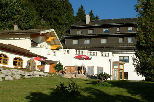 A picturesque building surrounded by green meadows and trees. On the terrace, there are umbrellas and furniture for relaxing.