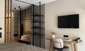 A modern room with a large bed, a desk, and a television on the wall. The room has a minimalist decor with warm colors and wooden details.