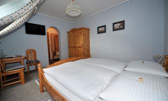 A cozy bedroom with a double bed and a large window. A wooden table and chairs complement the furnishings.
