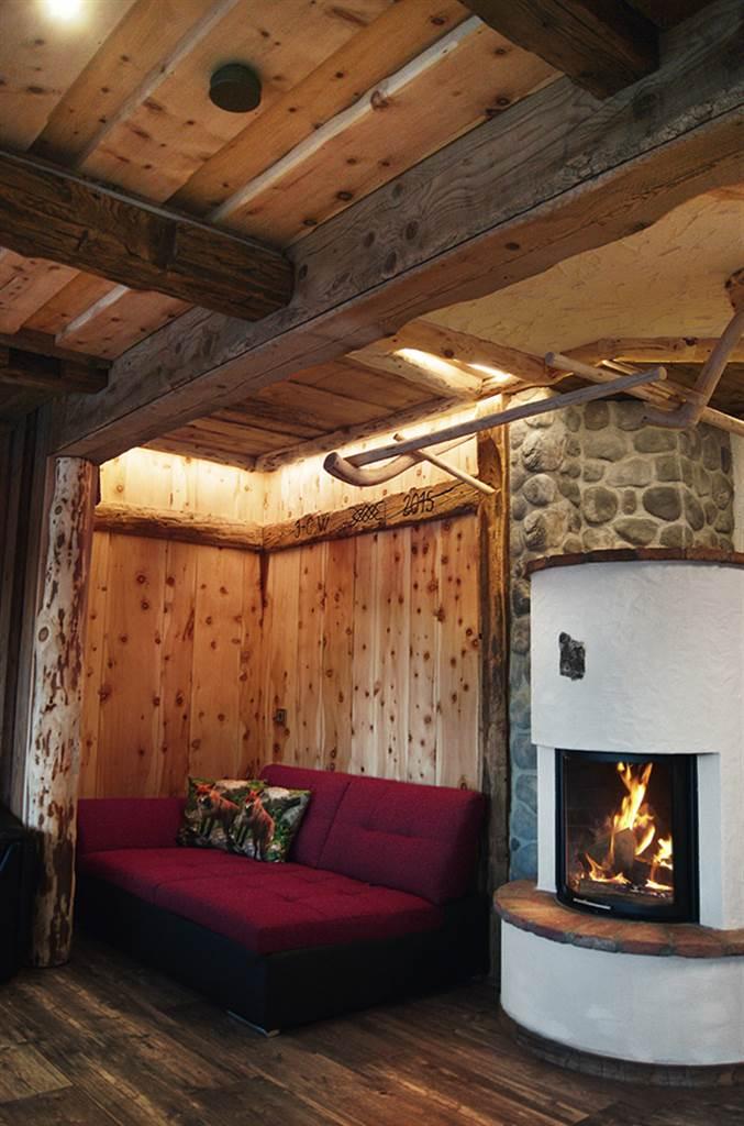 A cozy corner with a red sofa and an open fireplace. The walls are made of wood, giving the room a warm atmosphere.