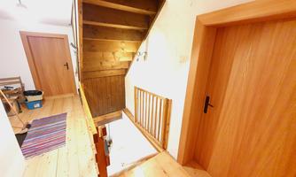 A bright hallway with a wooden staircase and wooden floor. There are two doors and a window on the wall.