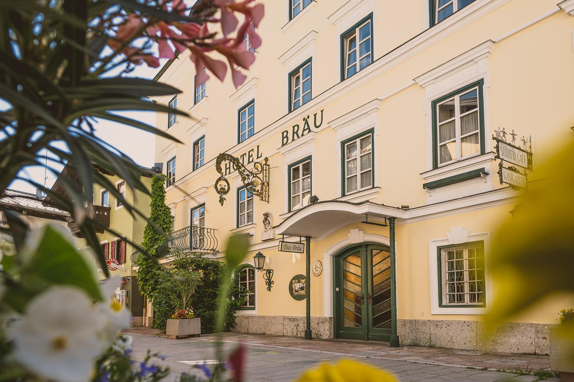 A lovely hotel named "Hotel Bräu" in soft shades of yellow. The facade is surrounded by flowers and plants.