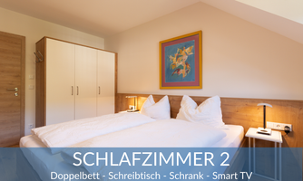 A modern bedroom with a double bed and a desk. There is a wardrobe and a smart TV, as well as a colorful picture on the wall.