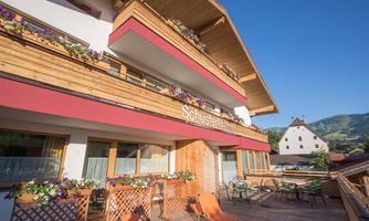 An inviting hotel with wooden cladding and flower boxes. Comfortable chairs and tables on the terrace overlook the mountains.