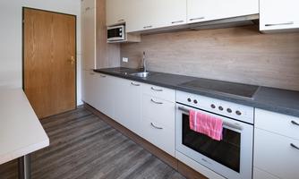 A modern kitchen with light cabinets and a dark countertop. The image shows a stove, a sink, and a microwave.