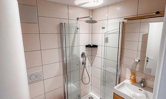 A modern bathroom with a glass shower and minimalist design. The white tiles and the wooden sink create a bright and inviting atmosphere.