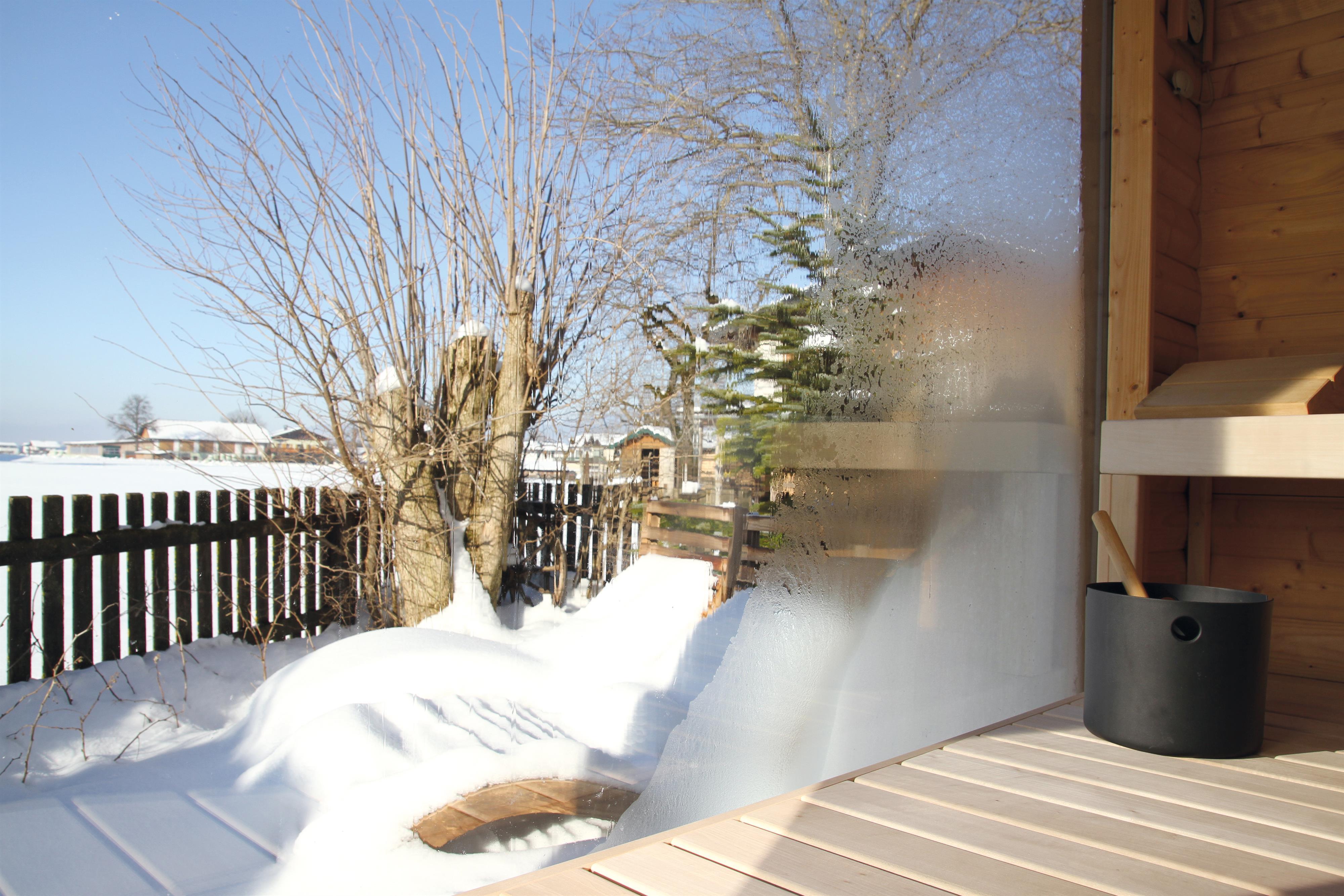 A snow-covered landscape with trees and a privacy screen. In the foreground, there is a wooden staircase and a bucket visible.