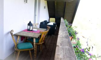 A cozy balcony with a wooden table and colorful chairs. The flower boxes add color and an inviting atmosphere.