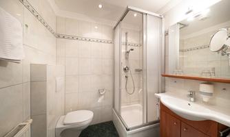 A modern bathroom with a shower, a sink, and a toilet. The walls are tiled and there is also a large mirror.