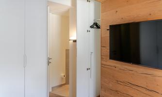A modern room with a minimalist design. On the wall hangs a flat-screen TV, and there is a practical wardrobe.