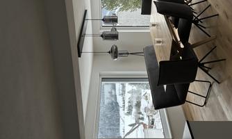 A modern dining area with a large wooden table and elegant black chairs. Large windows offer a view of a snow-covered landscape.