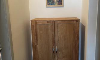 A wooden cabinet stands in a bright room. Above the cabinet hangs a colorful painting.
