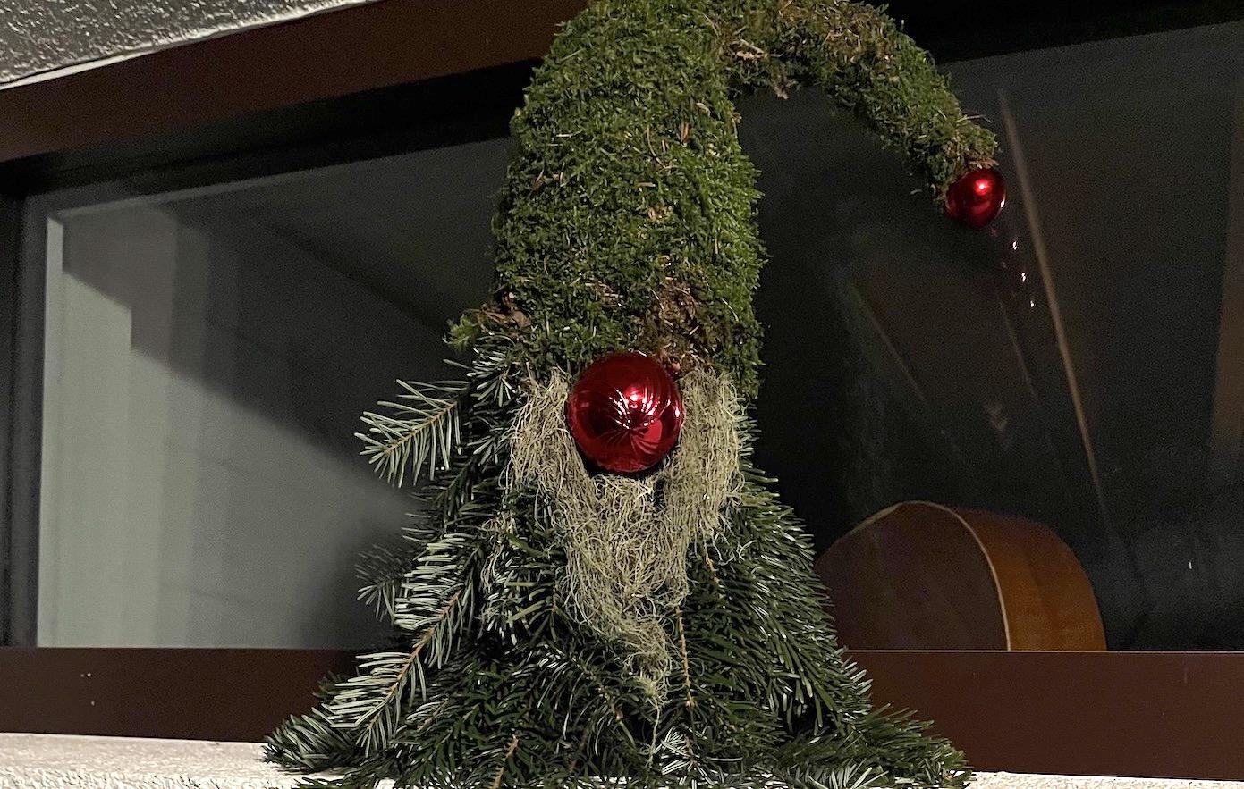 A decorative figure in the form of a Santa Claus, covered with moss. Red Christmas balls add a festive accent to the artwork.