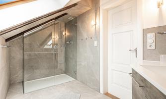 A modern bathroom with a glass shower and elegant tiled floor. The skylight provides plenty of natural light and a pleasant atmosphere.