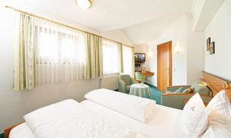 A bright and inviting hotel room with two beds and cozy seating. The room has large windows that let in plenty of daylight.