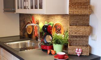 A modern kitchen with a sink, a blender, and fresh ingredients. On the wall, vegetables and fruits are decoratively depicted, and there is a plant as well as storage baskets.