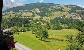 A picturesque landscape with gentle hills and lush greenery. In the background, mountains and a blue sky can be seen.