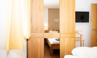 A cozy room with wooden paneling and a television on the wall. Through the doors, another bed can be seen.