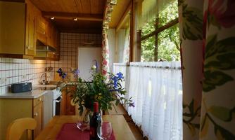 A bright kitchen with wooden cabinets and large windows. On the table, there is a bottle of wine and glasses, as well as fresh flowers in a vase.