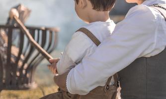 A mother sits with her child and gazes into the distance. In the background, a campfire is burning.