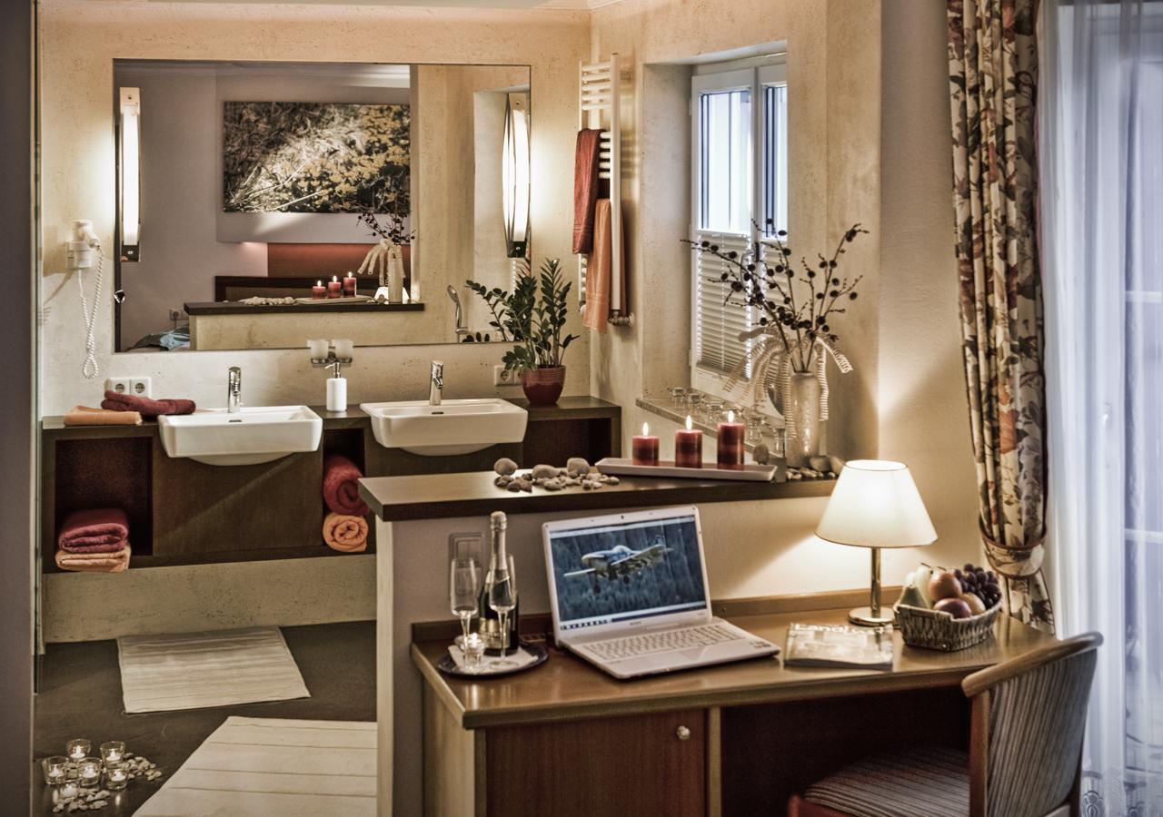 An elegant bathroom with two sinks and modern lamps. A sideboard with a laptop and several decorative elements creates a cozy atmosphere.