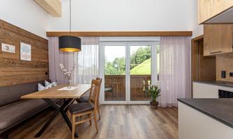 A modern dining room with wooden paneling and large windows. The space is bright and friendly, featuring a dining table and a cozy seating area.
