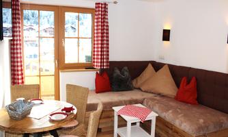 A cozy living space with a large sofa and a wooden table. Large windows provide plenty of daylight and a view of the surroundings.