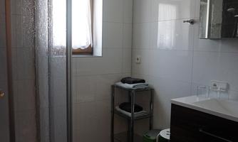 A modern bathroom with a shower cabin and a sink. It has bright tiles and a large window that provides plenty of light.