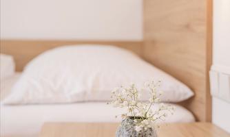A cozy bedroom with a wooden headboard and a nightstand. On the table sits a small vase with fresh flowers.