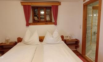 A cozy bedroom with a double bed and two large pillows. In the background, a window and an adjoining bathroom are visible.