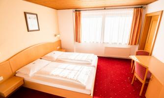 A bright hotel room with two single beds and a desk.  
Large windows provide plenty of daylight and a cozy atmosphere.