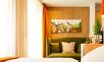 A bright room with a cozy green sofa and large windows. On the wall hangs a picture of deer in nature.