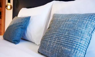 A cozy bed with white pillows and blue decorative pillows. The modern decor creates a relaxing atmosphere.