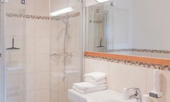 A modern bathroom with a shower and a floor-to-ceiling mirror. White towels are placed on the sink.