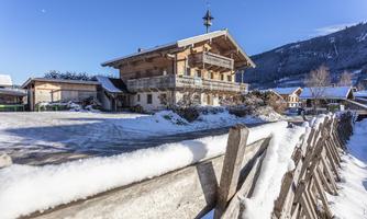 A cozy wooden house in the snow with a clear blue sky. In the foreground, you can see a fence and the beautiful winter landscape.