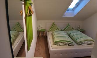 A cozy bedroom with a double bed and green bedding. The room has a window and a simple, modern style.