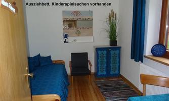 A blue room with a pull-out bed and a cozy chair.  
Ceilings and curtains in blue, along with a green plant, give the space an inviting atmosphere.