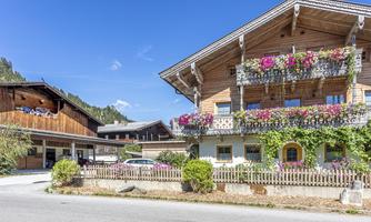 A traditional alpine wooden house with beautiful balconies and colorful flowers. In the background, a picturesque mountain landscape can be seen.