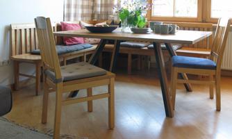 A cozy dining area with a table and several wooden chairs. On the table, there are dishes and a floral arrangement.