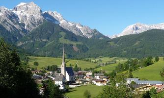A picturesque village view surrounded by high mountains. The church with its tall tower is the focal point of the landscape.