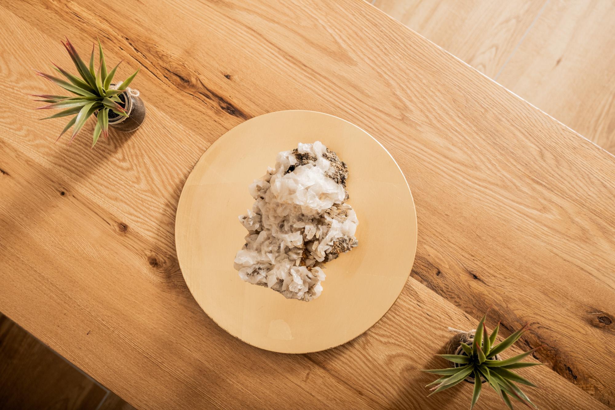 A plate with a portion of rice and a white sauce is on a wooden table. Next to it are two small plants.