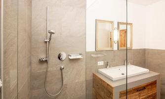 A modern bathroom with a rain shower and a stylish wooden sink unit. The walls are in neutral shades of gray.