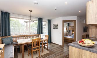 A modern kitchenette with a wooden dining area and comfortable chairs. The room is bright and welcoming, with large windows and a pleasant atmosphere.