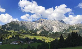 An impressive mountain landscape with majestic peaks and green grass. The sky is clear with some white clouds.