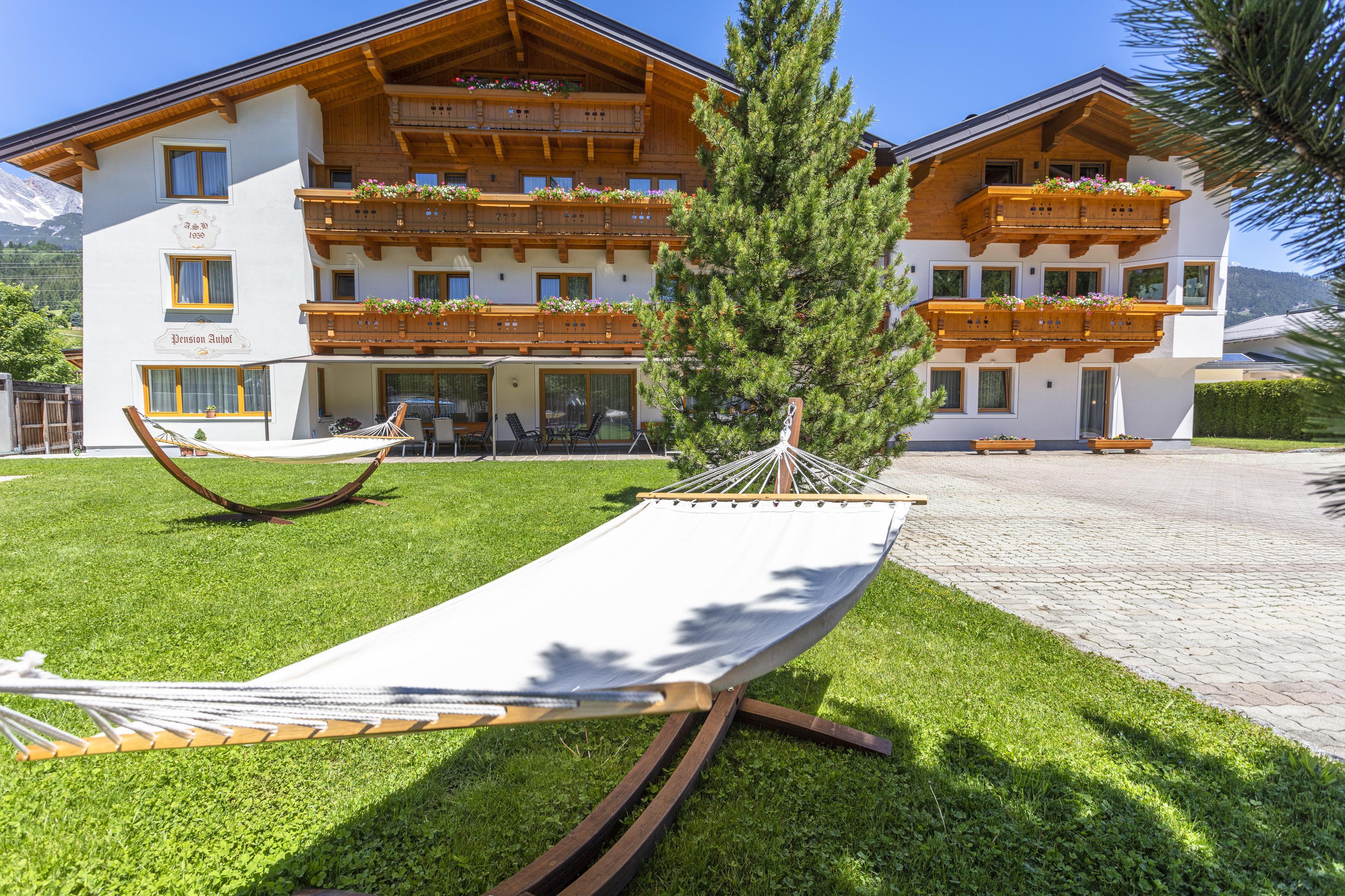 A cozy accommodation with wooden decorations and balconies. In the foreground, there is a hammock on the green lawn.