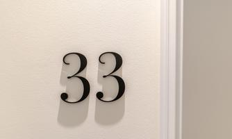 An elegant house number 33 in cursive script. It is located on a bright wall.