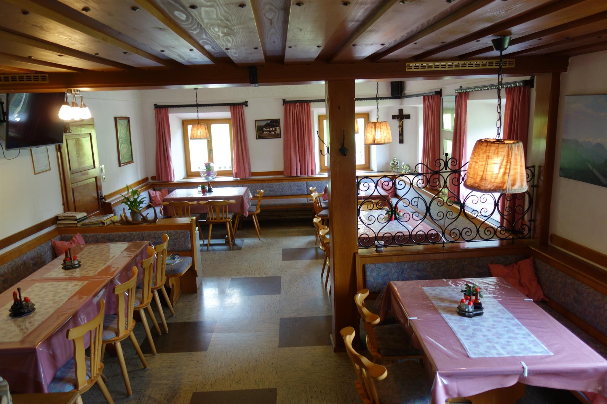 A cozy restaurant with a wooden ceiling and tables covered with pink tablecloths. The windows are adorned with curtains and the atmosphere is inviting.