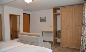 A simple room with two beds and a comfortable couch. There is a wooden wardrobe and a table, as well as a window with a curtain.